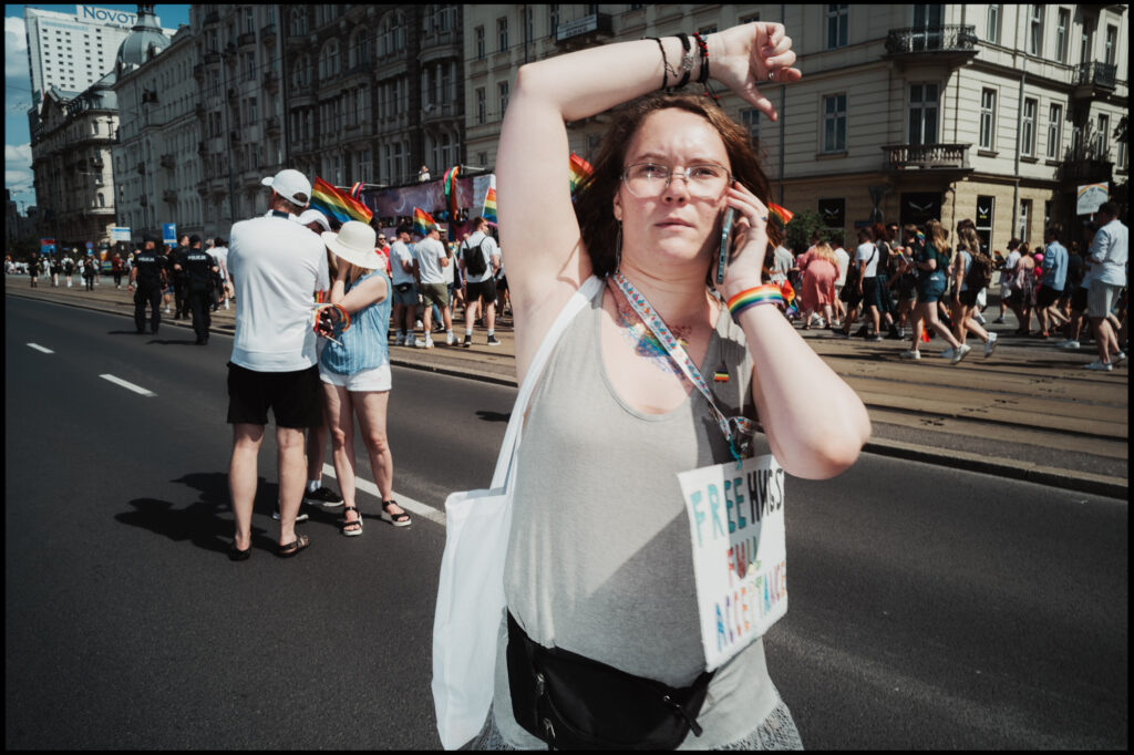 A participant marches down the street during Warsaw Pride 2024 while talking on the phone, waving their free hand in the air with a focused expression.